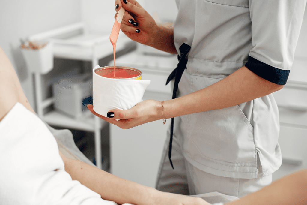 A woman sitting in a salon chair while a therapist works with wax.