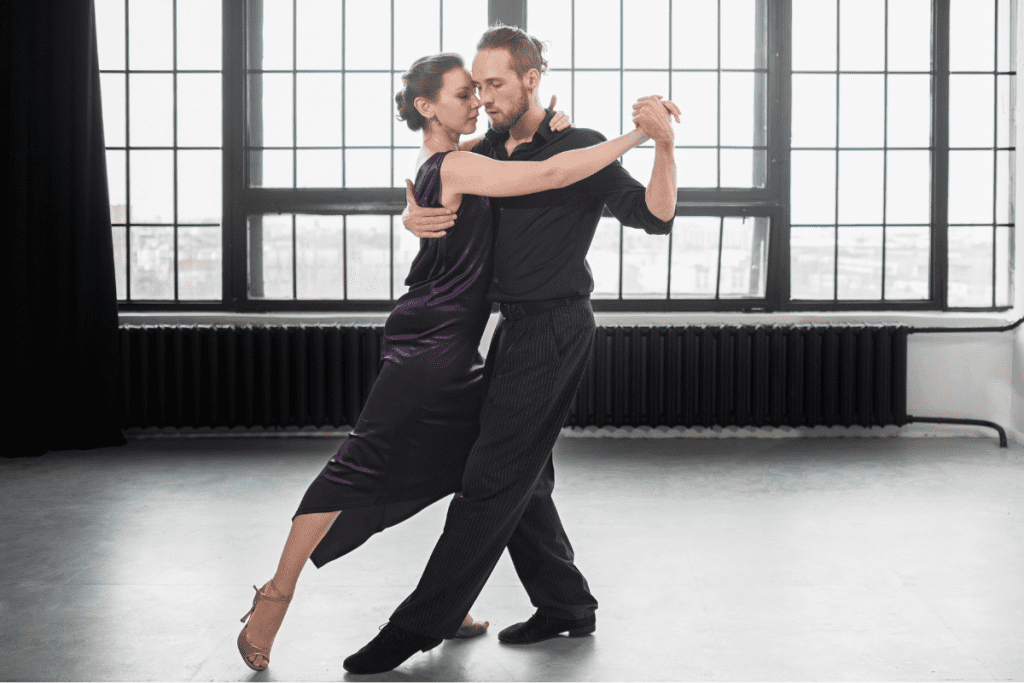 A couple gracefully dancing together in a spacious, empty room with soft lighting.