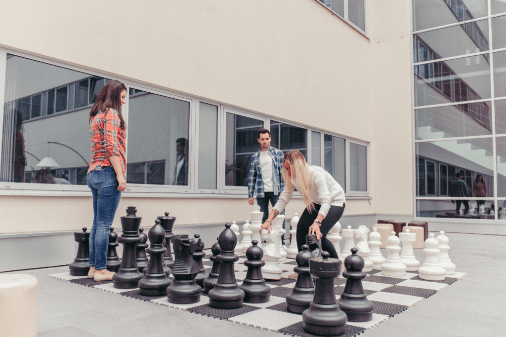 Three individuals engaged in a chess game on a large outdoor chessboard, focused on their next moves.