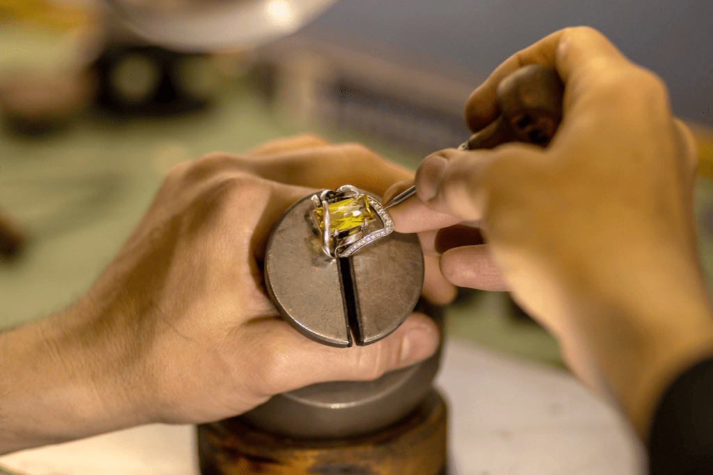 A man carefully crafts a ring featuring a prominent yellow stone, focused on his intricate work.