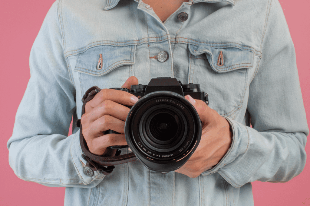 A woman in a denim jacket holds a camera, ready to capture a moment.