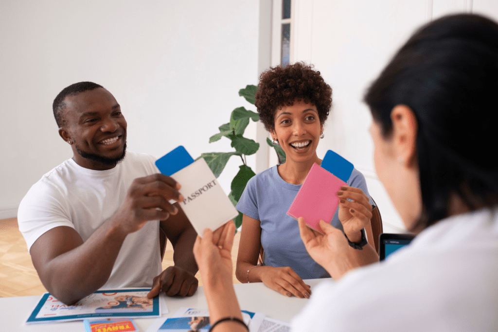 A travel agent and clients sit around a table, discussing travel plans while examining cards and passports.