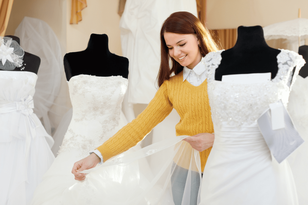 A woman examines wedding dresses displayed in a boutique store, surrounded by various styles and colors.
